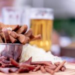 A close-up of a variety of pub snacks and a glass of beer on a wooden platter, perfect for an appetizer.