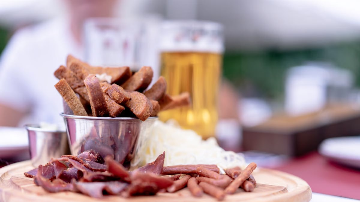 A close-up of a variety of pub snacks and a glass of beer on a wooden platter, perfect for an appetizer.